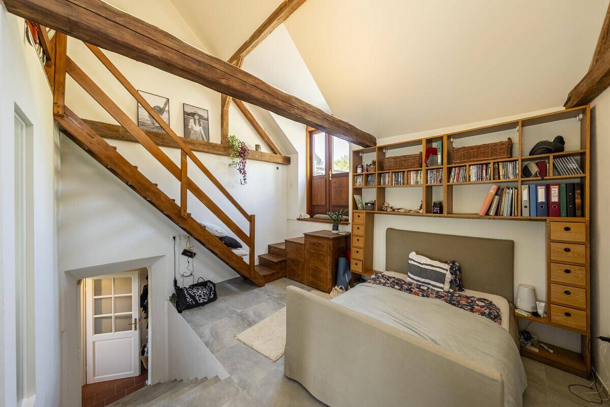 Offenes Schlafzimmer im Loft-Stil mit hohen Decken, sichtbaren Holzbalken und einer Holztreppe.