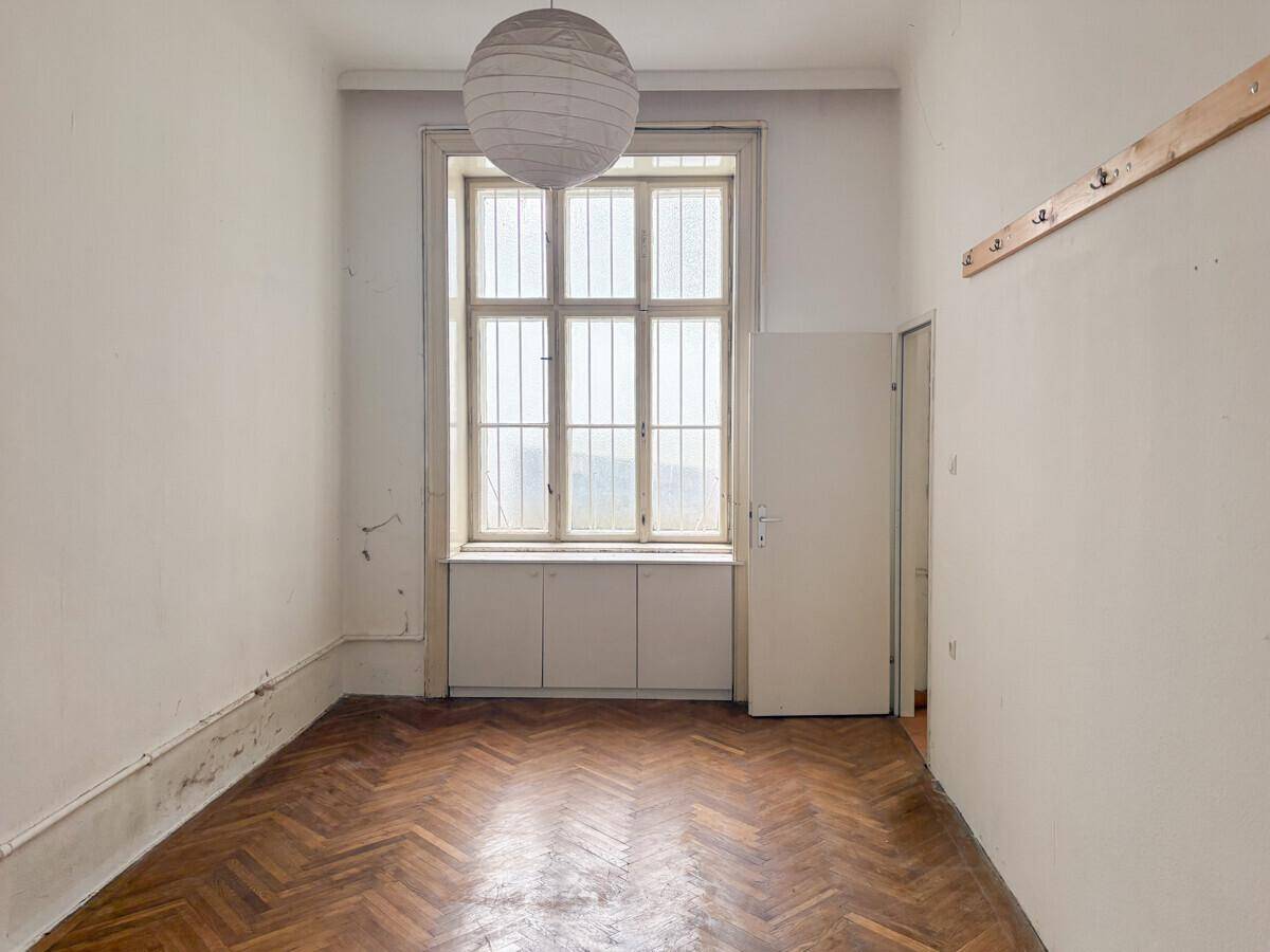 Heller Raum mit Fischgrätparkett, einem großen Fenster mit Gitter und einer Papierlampe.