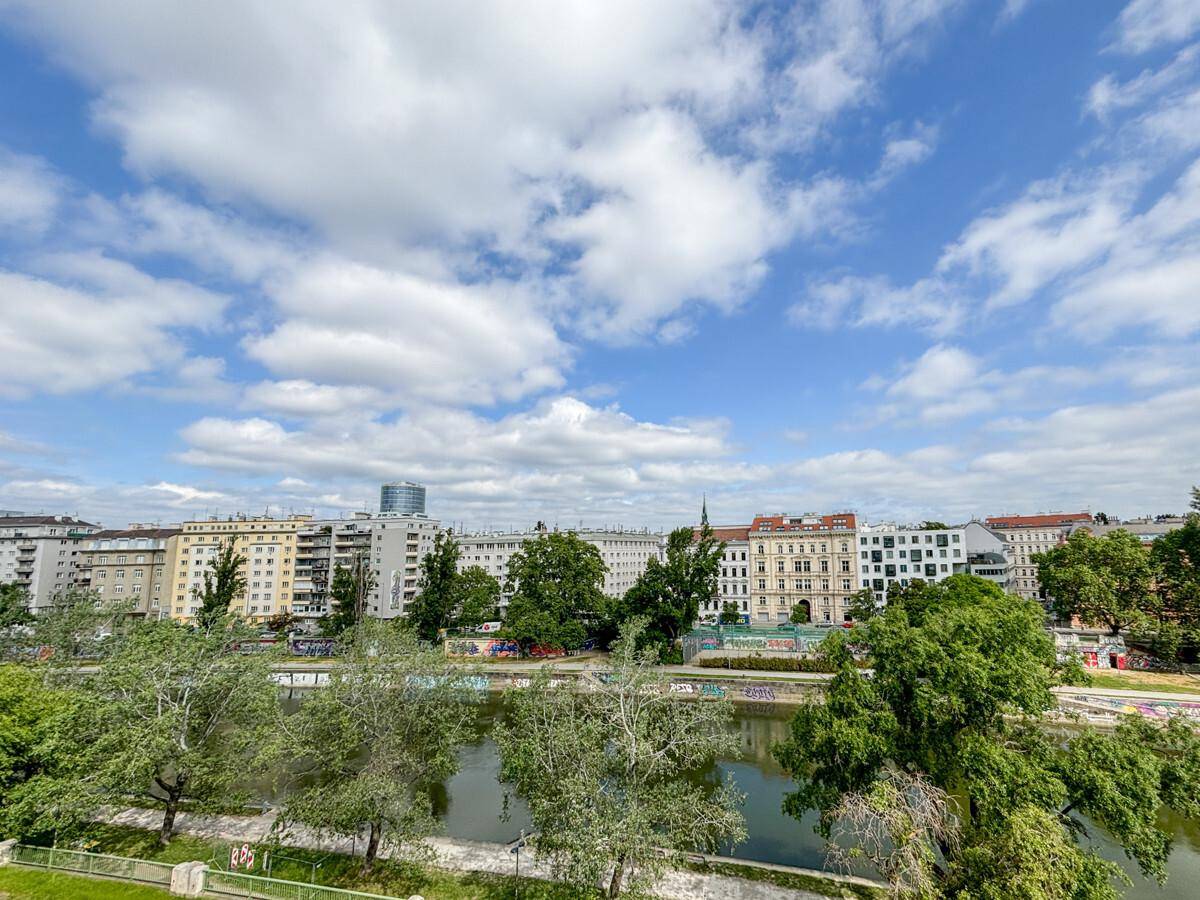 Weitläufiger Blick über den Fluss und die Stadt mit vielen Bäumen und Gebäuden im Hintergrund.