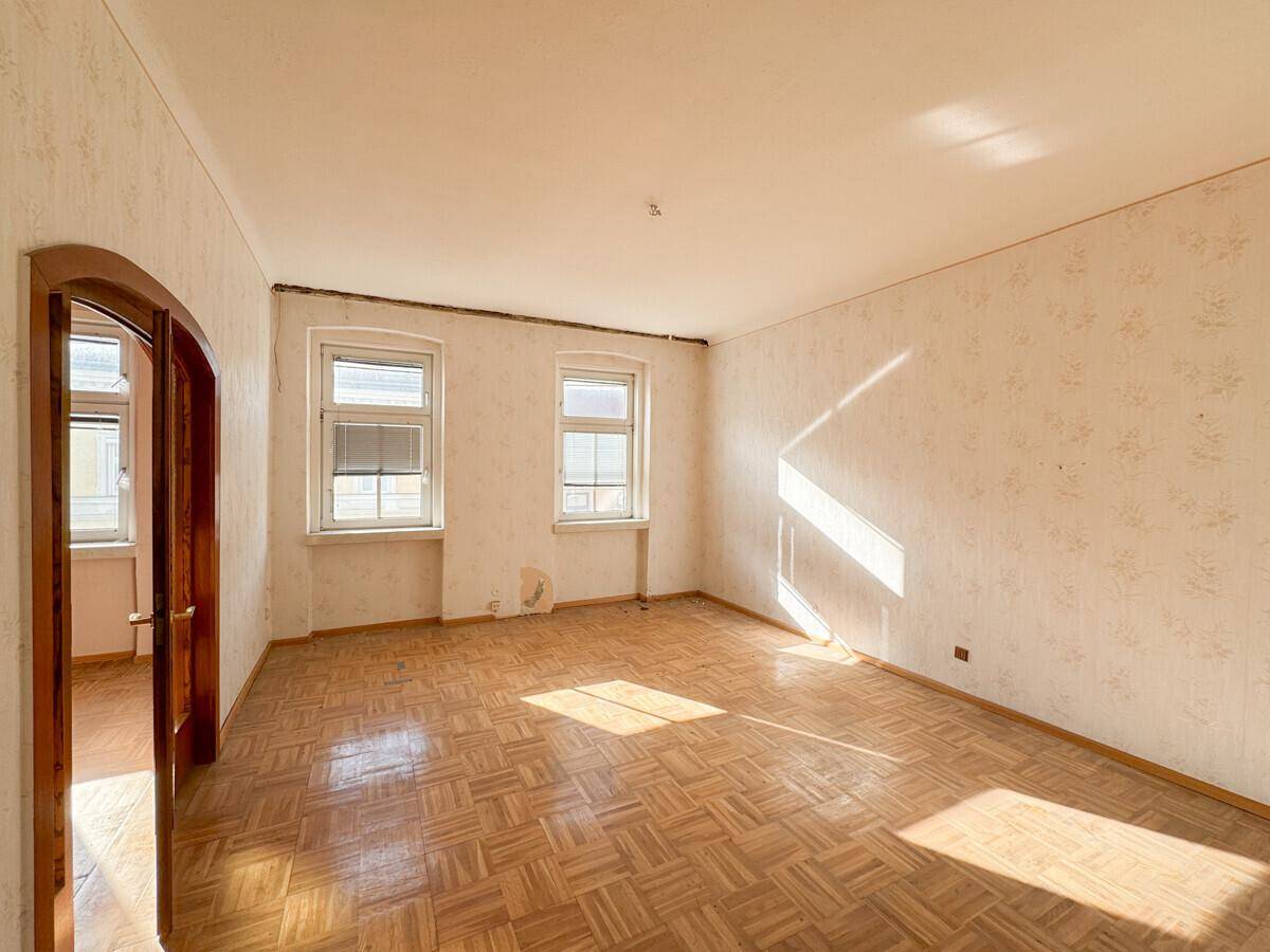 Leeres Zimmer mit Fischgrätparkett und Tapetenresten, bereit für eine Renovierung.