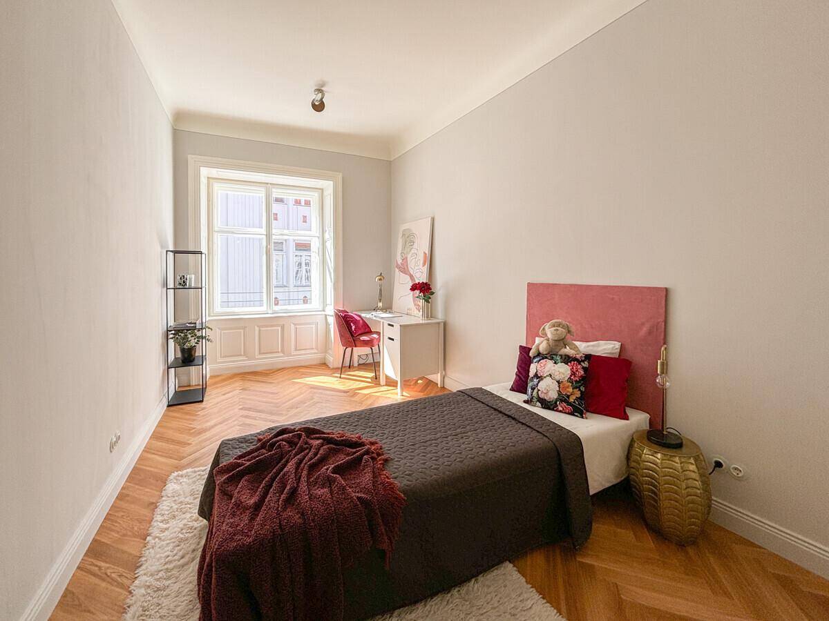 Helles Kinder- oder Gästezimmer mit Einzelbett, Schreibtisch und Fischgrätparkett.
