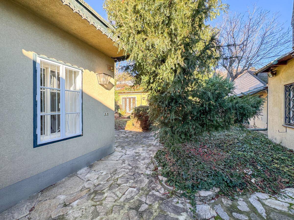 Steinweg führt durch den grünen Garten entlang der Hausfassade mit klassischen Fenstern.