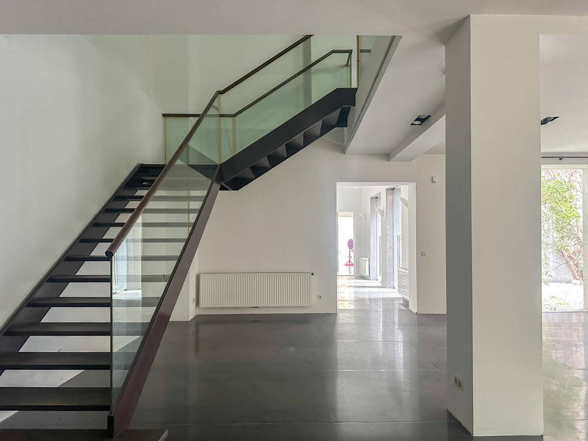 Moderne Treppe mit Glasgeländer und dunklen Stufen in einem hellen, offenen Raum mit Betonboden.