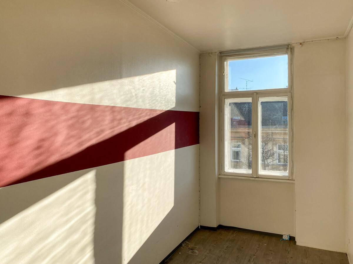 Heller Raum mit rotem Wandstreifen und einem Fenster, das viel Tageslicht spendet.
