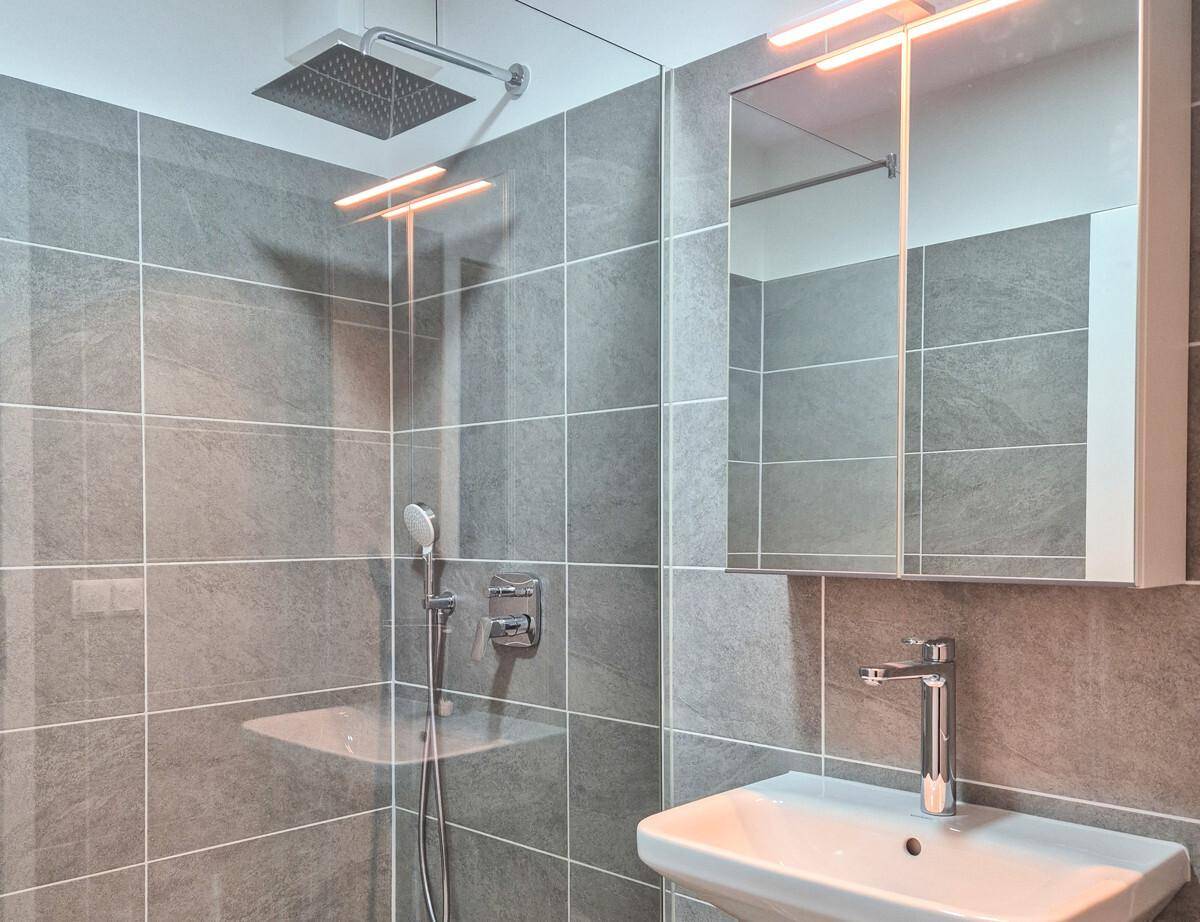 Modernes Badezimmer mit großformatigen grauen Fliesen, Regendusche und Waschtisch mit Spiegelschrank.