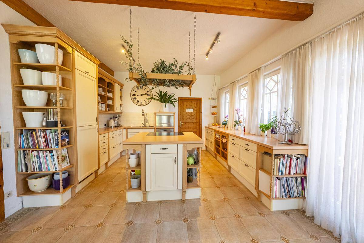Helle Landhausküche mit Holzfronten, Kücheninsel und viel Stauraum, durchflutet von Tageslicht.