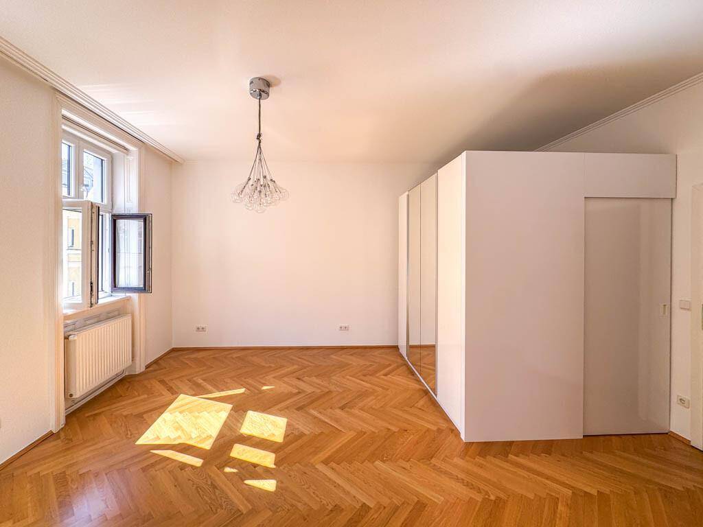 Geräumiges Zimmer mit Fischgrätparkett, einem großen Spiegelschrank und viel natürlichem Lichteinfall.