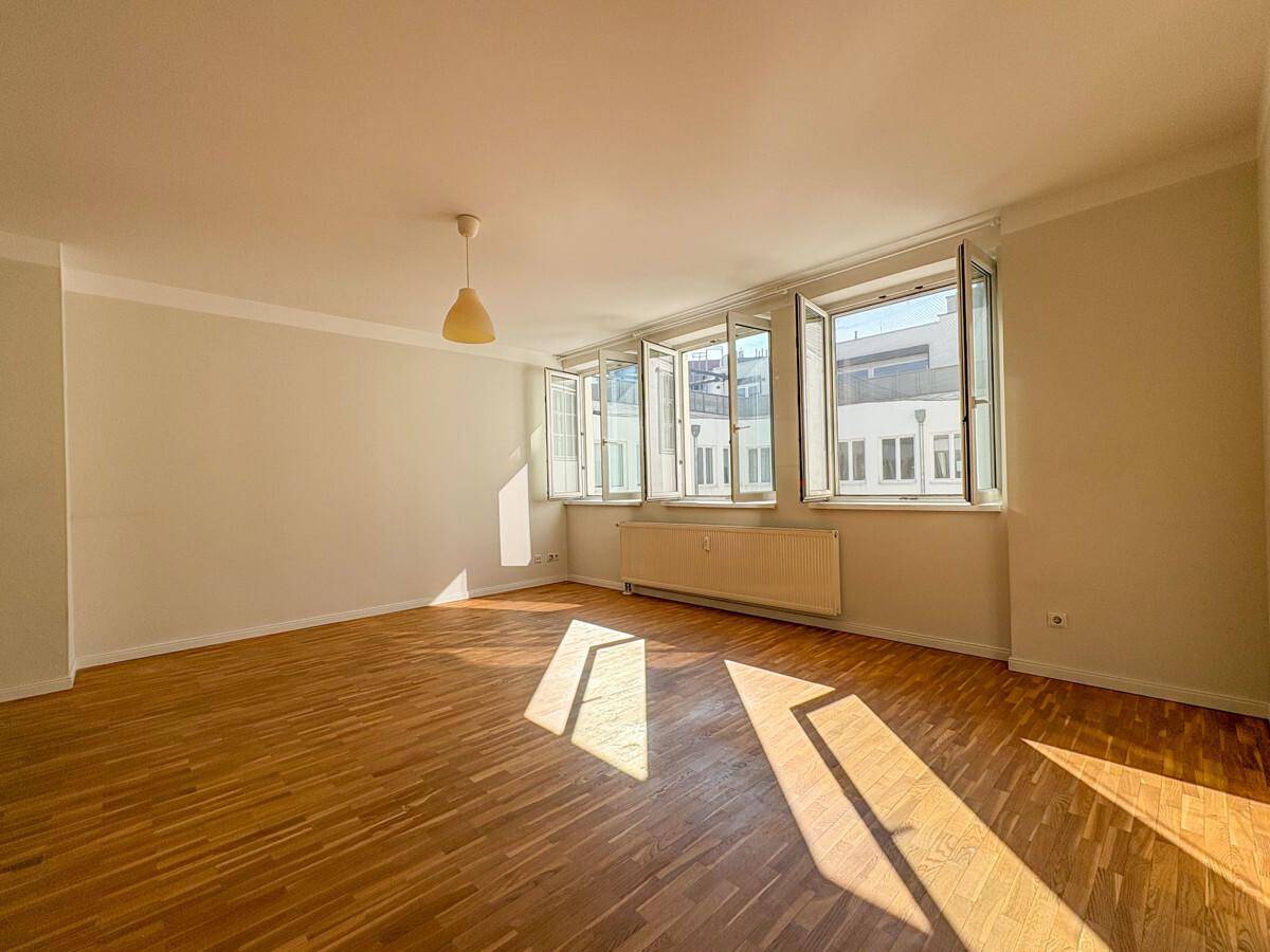 Geräumiger, heller Wohnraum mit Holzboden und großen Fenstern, die den Raum mit Sonnenlicht durchfluten.