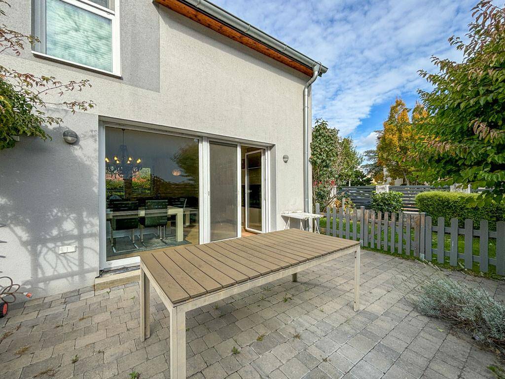Große gepflasterte Terrasse mit Esstisch im Freien und Blick in den Garten.