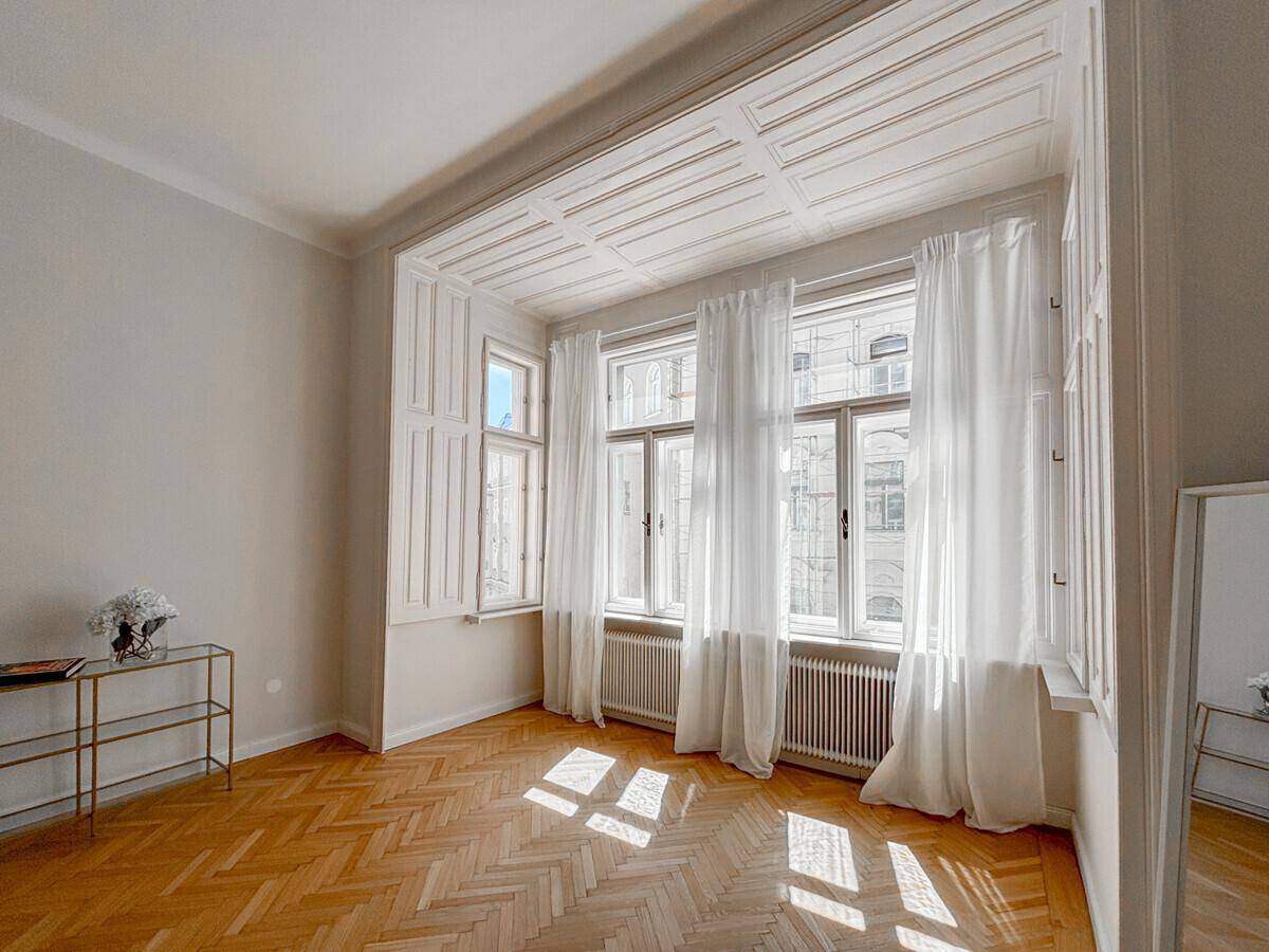 Heller Raum mit Fischgrätparkett, hohen Decken und einem dekorativen Erkerfenster.