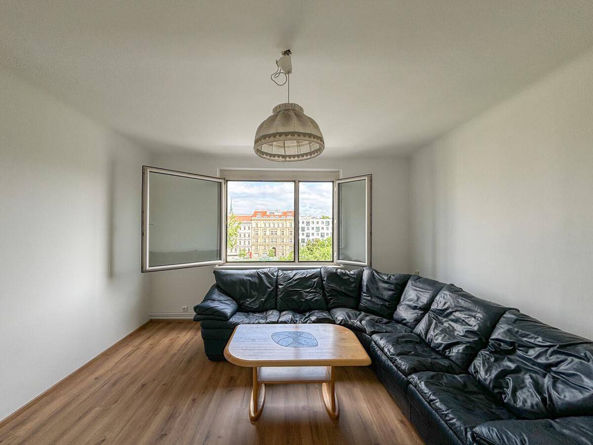 Wohnzimmer mit dunklem Ecksofa, Couchtisch und Blick auf die Stadt durch die geöffneten Fenster.