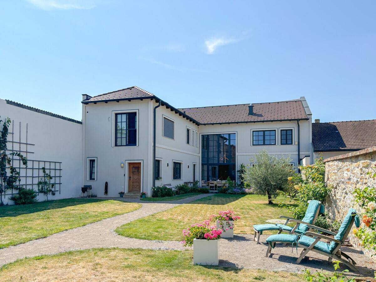 Ansicht des modernen Wohnhauses mit weitläufigem Garten und bequemen Gartenliegen unter blauem Himmel.