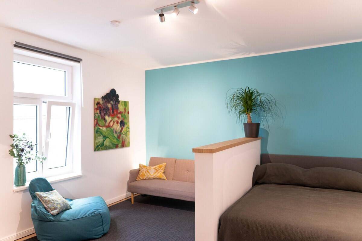 Heller Wohn- und Schlafbereich mit moderner Einrichtung, farbiger Wand und großem Fenster.