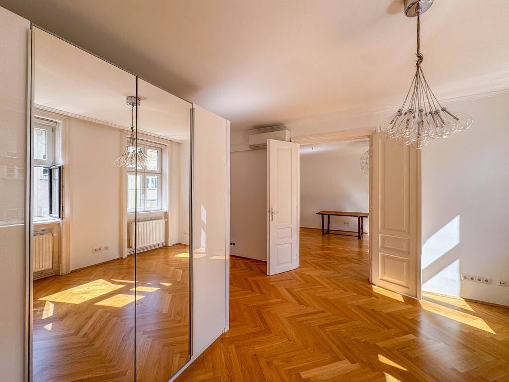 Helles Zimmer mit Fischgrätparkett und einem großen Spiegelschrank, der den Raum optisch vergrößert.