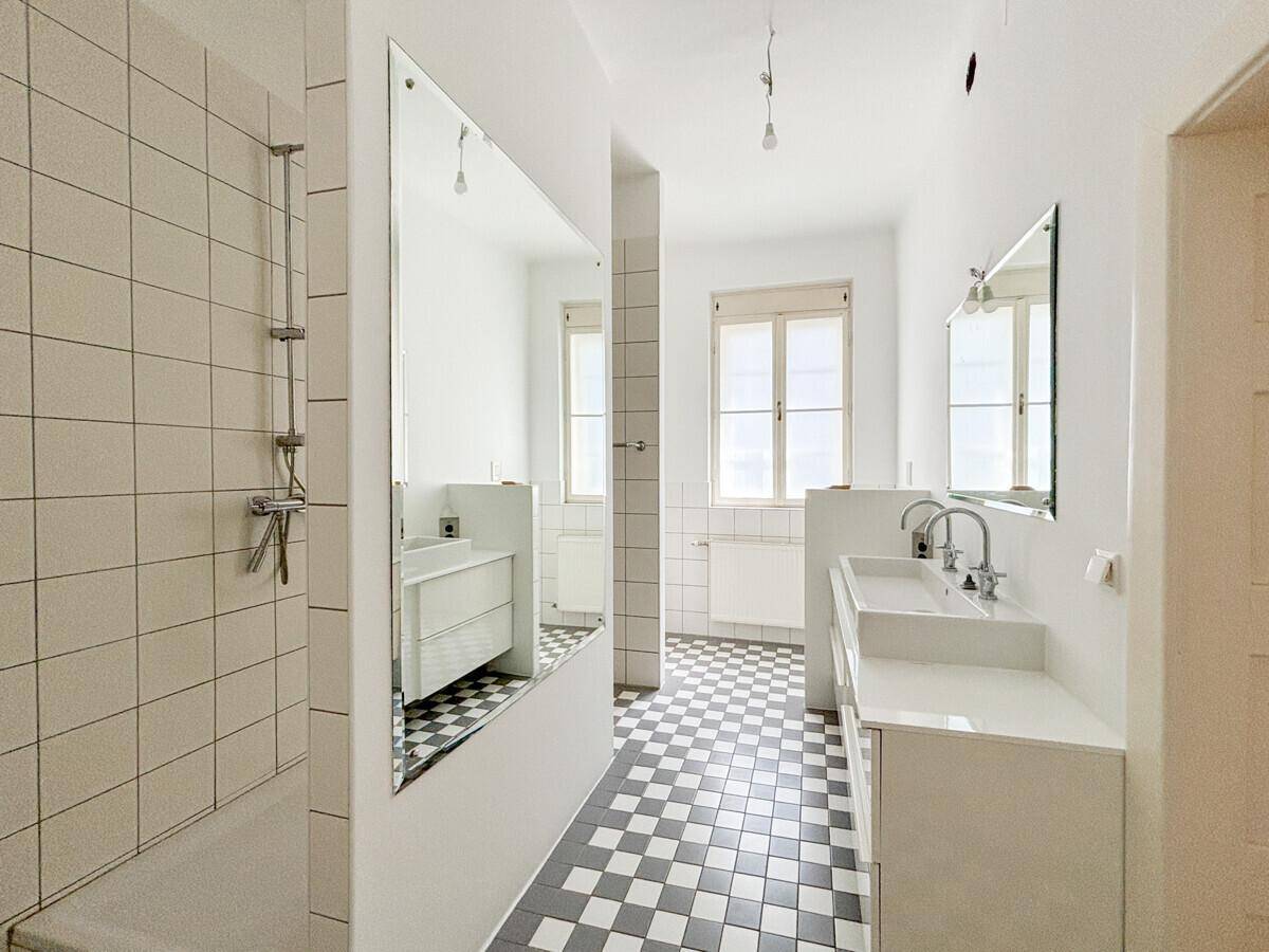 Modernes Badezimmer mit doppelten Waschbecken, großer Spiegelfläche und schwarz-weißem Fliesenboden.