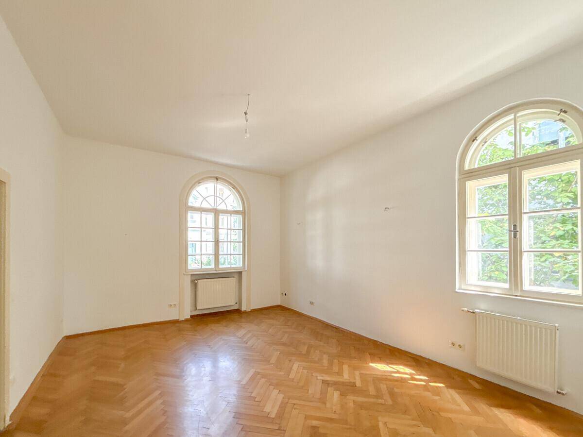 Geräumiges Zimmer mit Fischgrätparkett und eleganten Rundbogenfenstern.