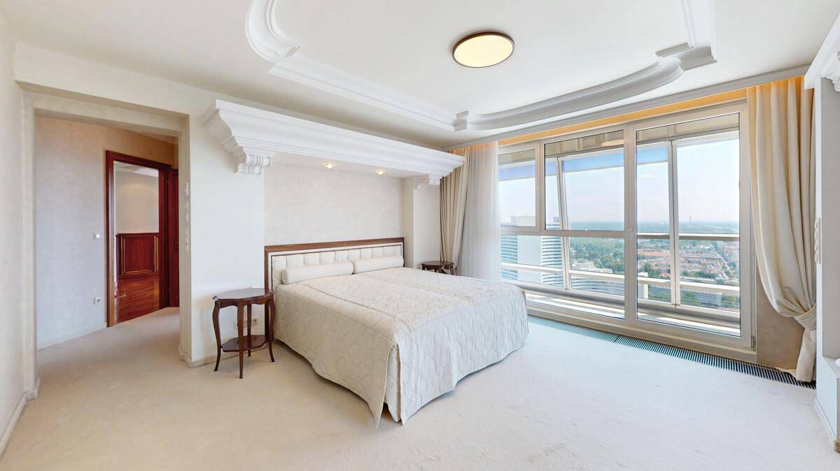 Helles Schlafzimmer mit Doppelbett, Teppichboden und großen Fenstern mit Aussicht.