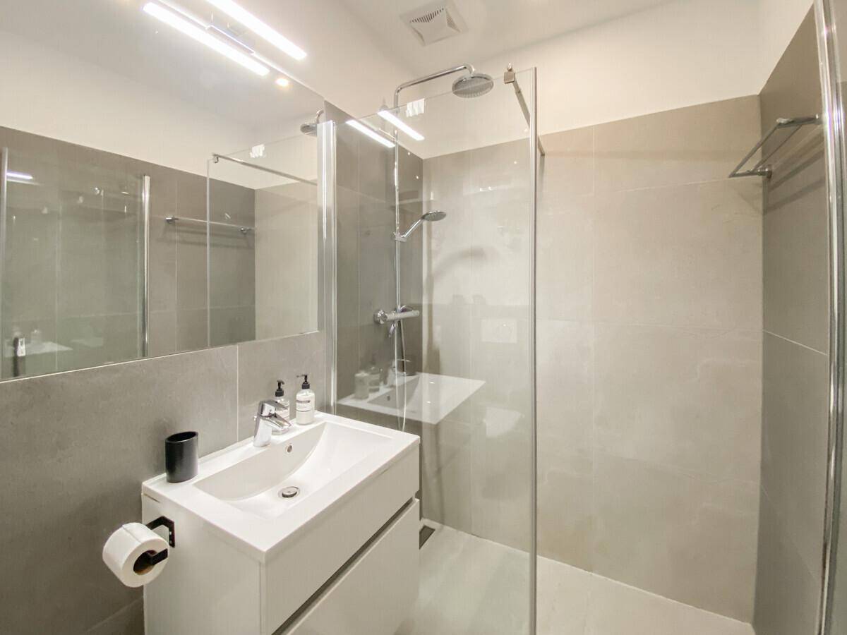 Modernes Badezimmer mit begehbarer Dusche, großem Spiegel und hellgrauen Fliesen.