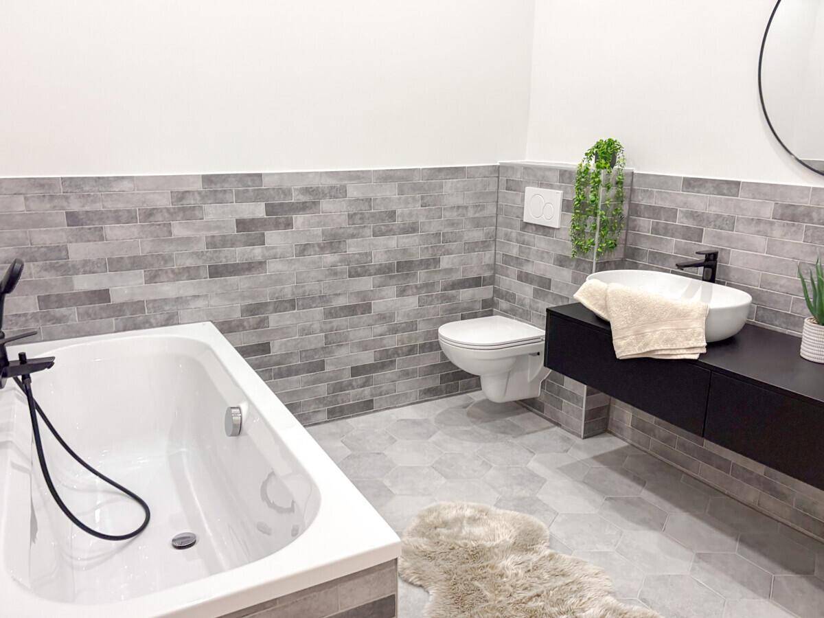 Modernes Badezimmer mit Badewanne, Wand-WC und stilvollen grauen Fliesen.