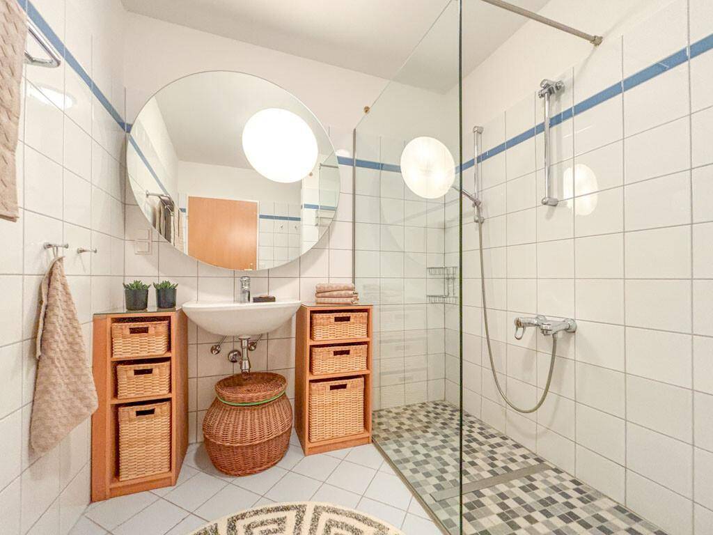 Funktionales Badezimmer mit Duschkabine, großem Spiegel und praktischen Holzregalen.