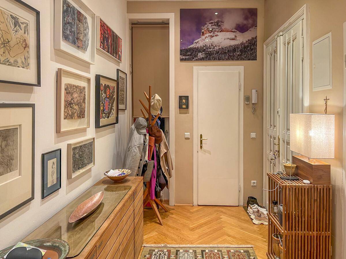 Heller Flur mit Fischgrätparkett, Garderobe und vielen gerahmten Kunstwerken.