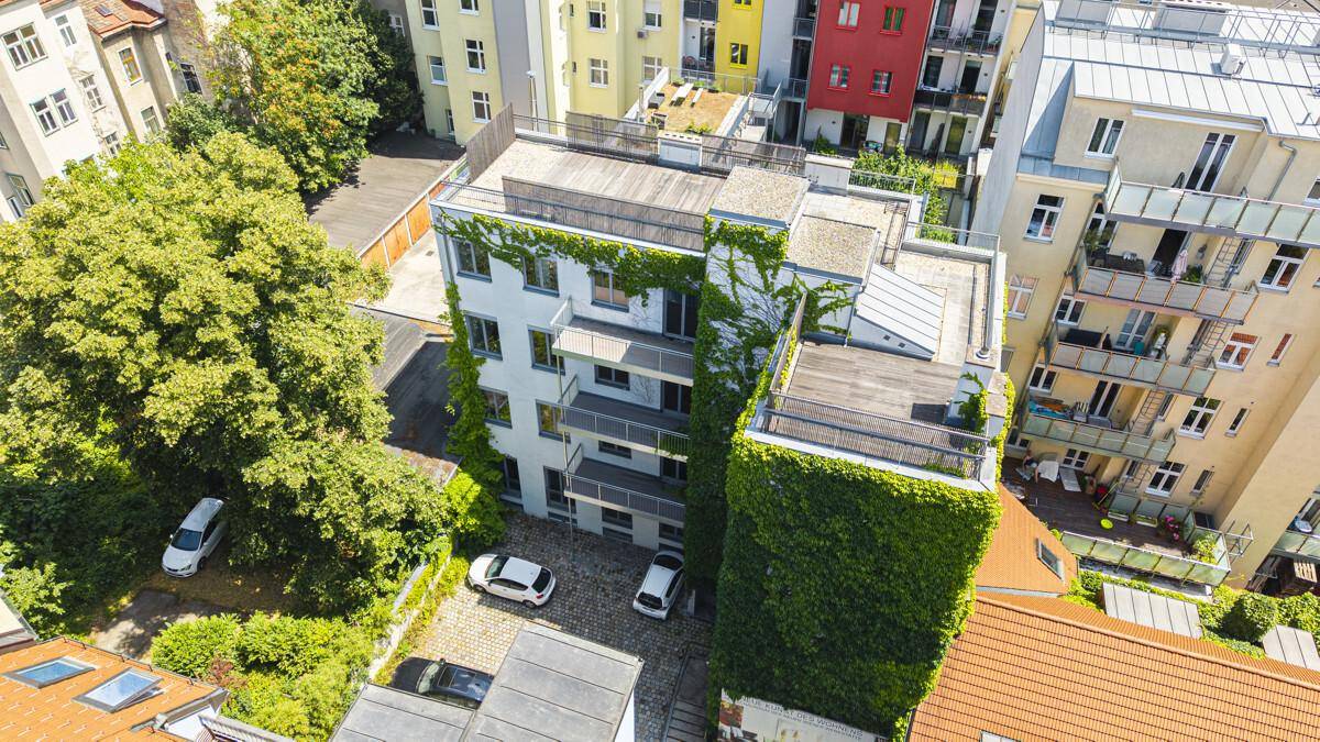 Luftaufnahme eines modernen Gebäudes mit begrünten Fassaden und Parkplätzen im Innenhof.