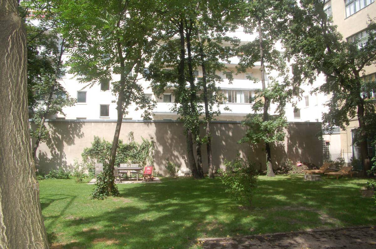 Grüner Gartenbereich mit Rasen, Bäumen und einer kleinen Sitzecke im Freien.