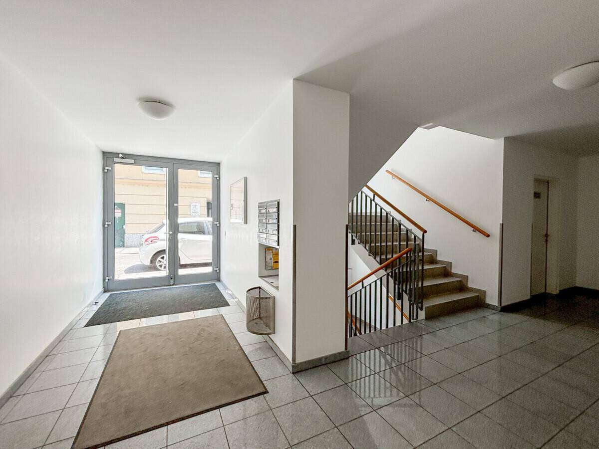 Heller Eingangsbereich des Gebäudes mit Treppenhaus und Zugang zur Straße.