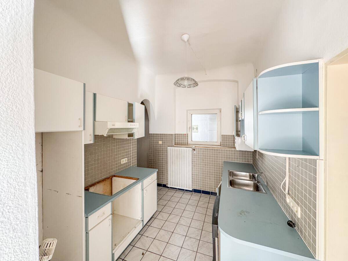 Alte Küche mit blauen Schränken und Fliesenboden, die eine umfassende Renovierung benötigt.