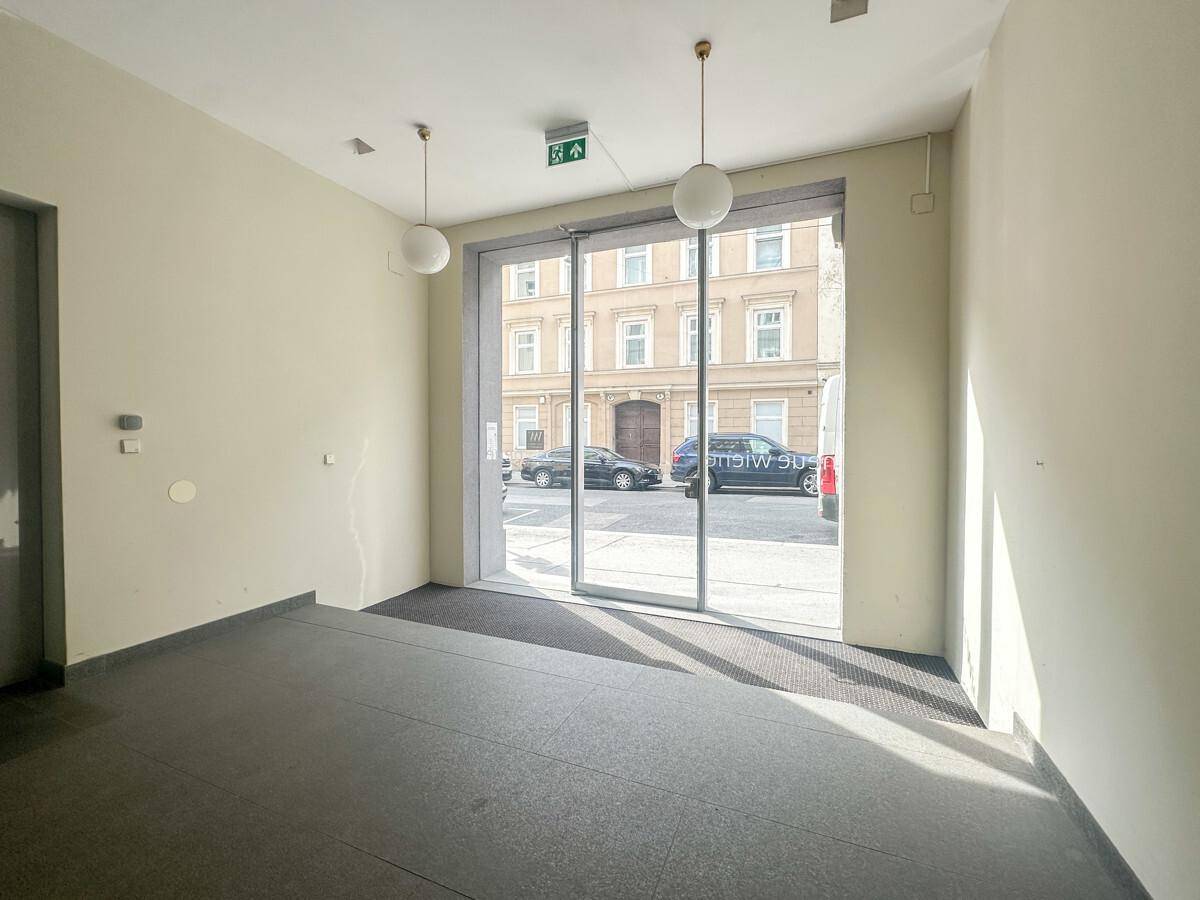 Heller Eingangsbereich mit großer Glastür, die einen Blick auf die Straße und gegenüberliegende Gebäude bietet.