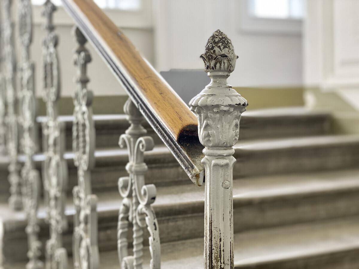 Detailaufnahme eines historischen Treppengeländers mit kunstvollen Verzierungen und Holzhandlauf.