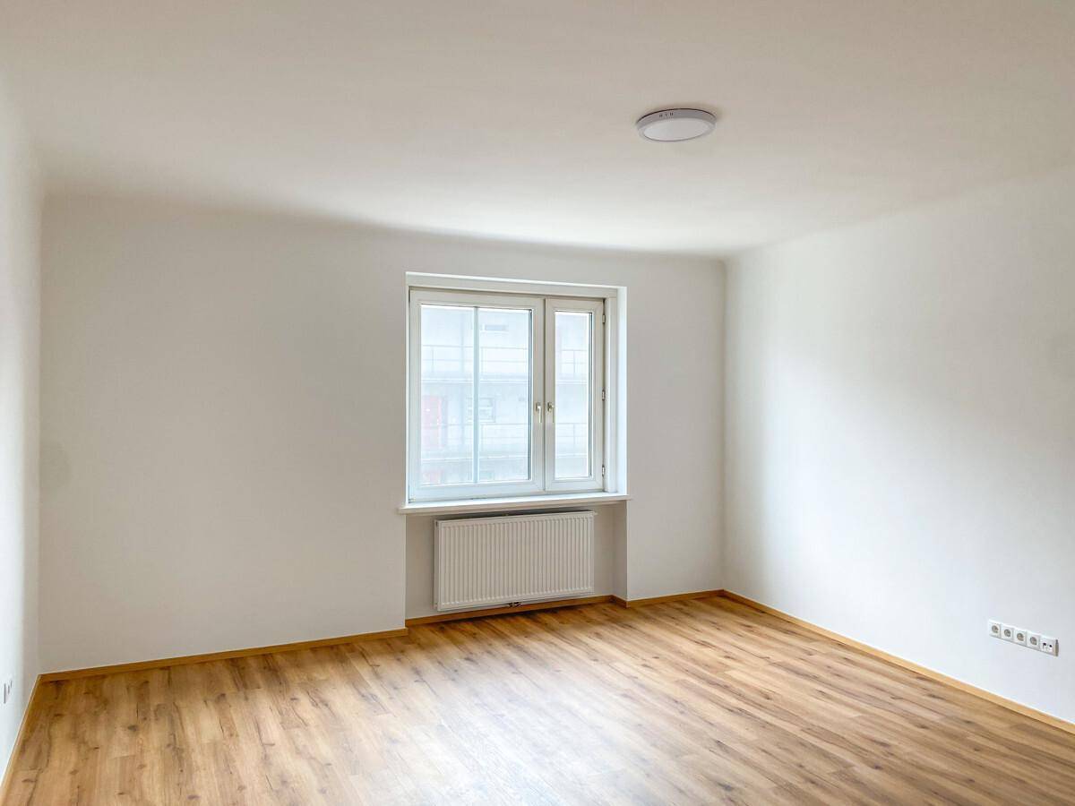 Leeres Zimmer mit großem Fenster, Heizkörper und neuem Laminatboden.