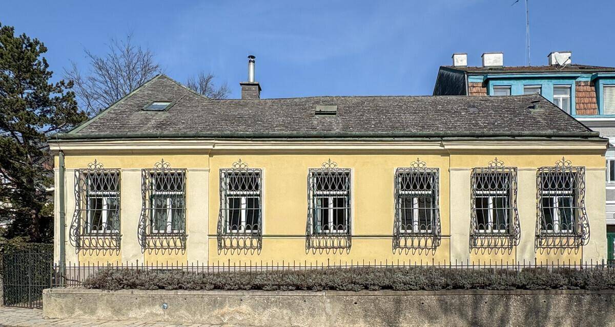 Klassische Fassade eines Einfamilienhauses mit gelbem Putz und dekorativen Fenstergittern.
