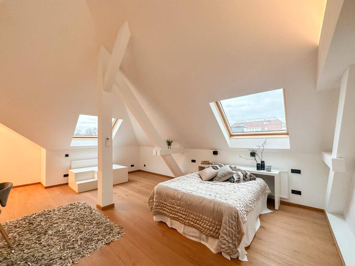 Helles Schlafzimmer im Dachgeschoss mit schrägen Wänden, Dachfenstern und warmem Holzboden.