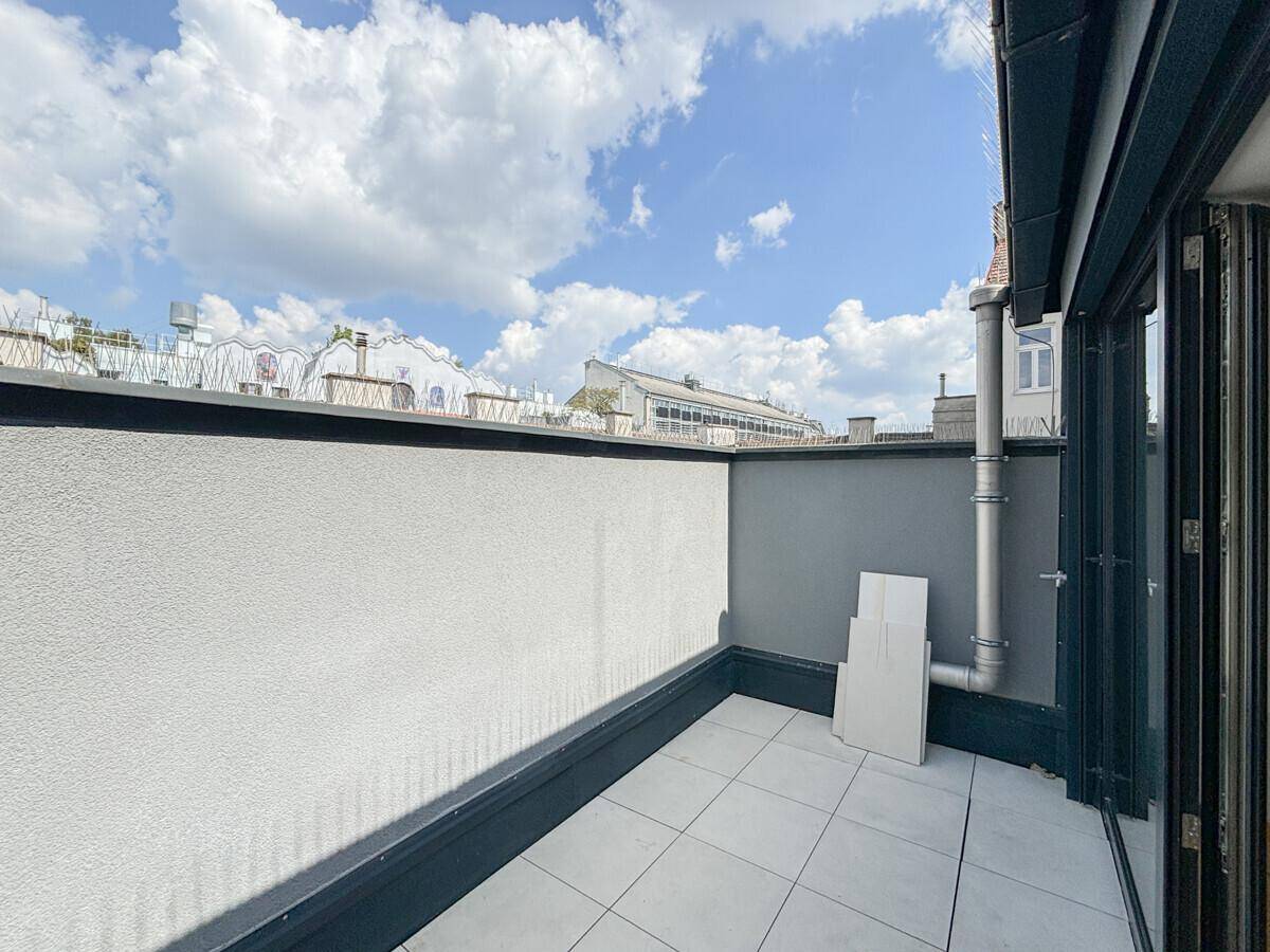 Sonniger Terrassenbereich mit Fliesenboden und Blick auf die umliegenden Dächer.