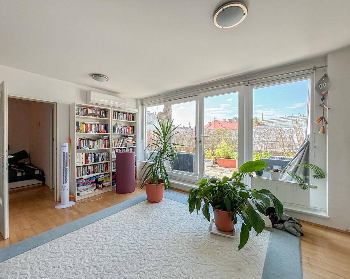 Heller Wohnraum mit großen Fenstern, Bücherregal und Zugang zu einer Terrasse.