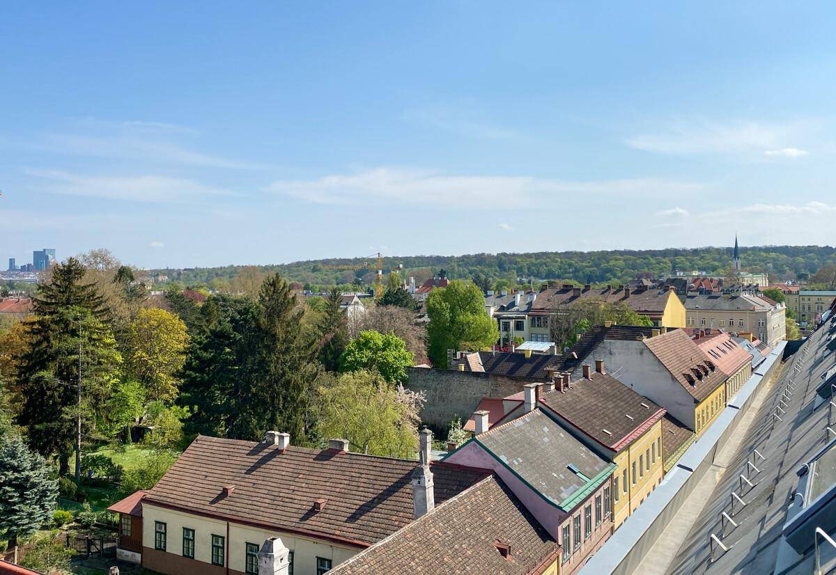 Panoramablick über die Dächer der Stadt und grüne Hügel unter blauem Himmel.