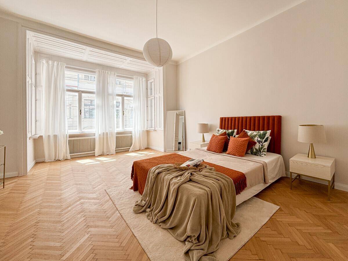 Helles Schlafzimmer mit Fischgrätparkett, großem Bett und einem charmanten Erkerfenster.