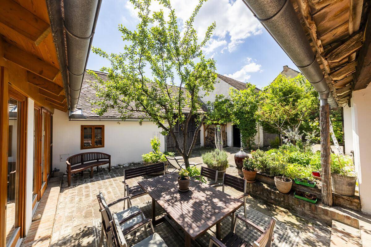 Sonniger Innenhof mit gepflastertem Bereich, Esstisch und Stühlen, umgeben von grünen Pflanzen.