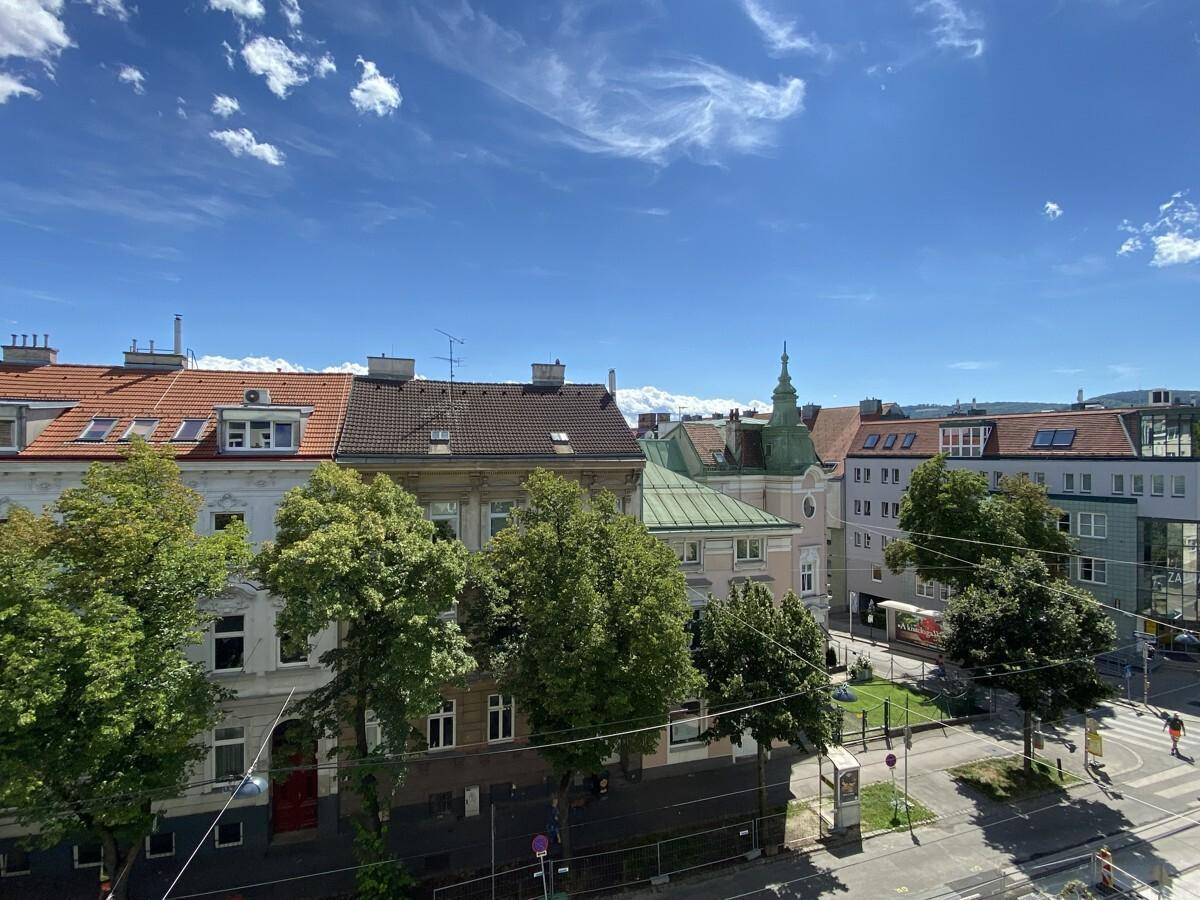 Weitblick über die Dächer der Stadt mit grünen Bäumen und blauem Himmel.