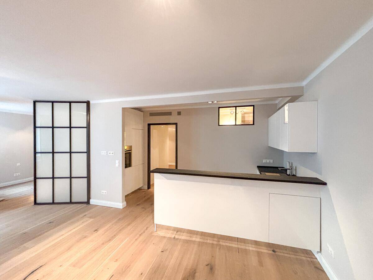 Moderner Wohnbereich mit integrierter Küchenzeile, dunkler Arbeitsplatte und eleganter Glas-Raumtrennung.