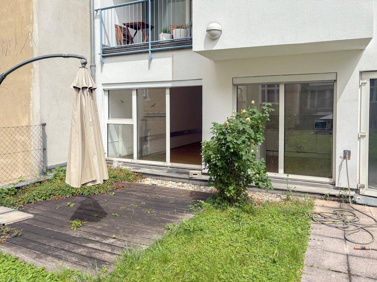 Terrasse mit Holzdeck und Rasenfläche, direkt zugänglich von den Innenräumen, mit einem großen Sonnenschirm.