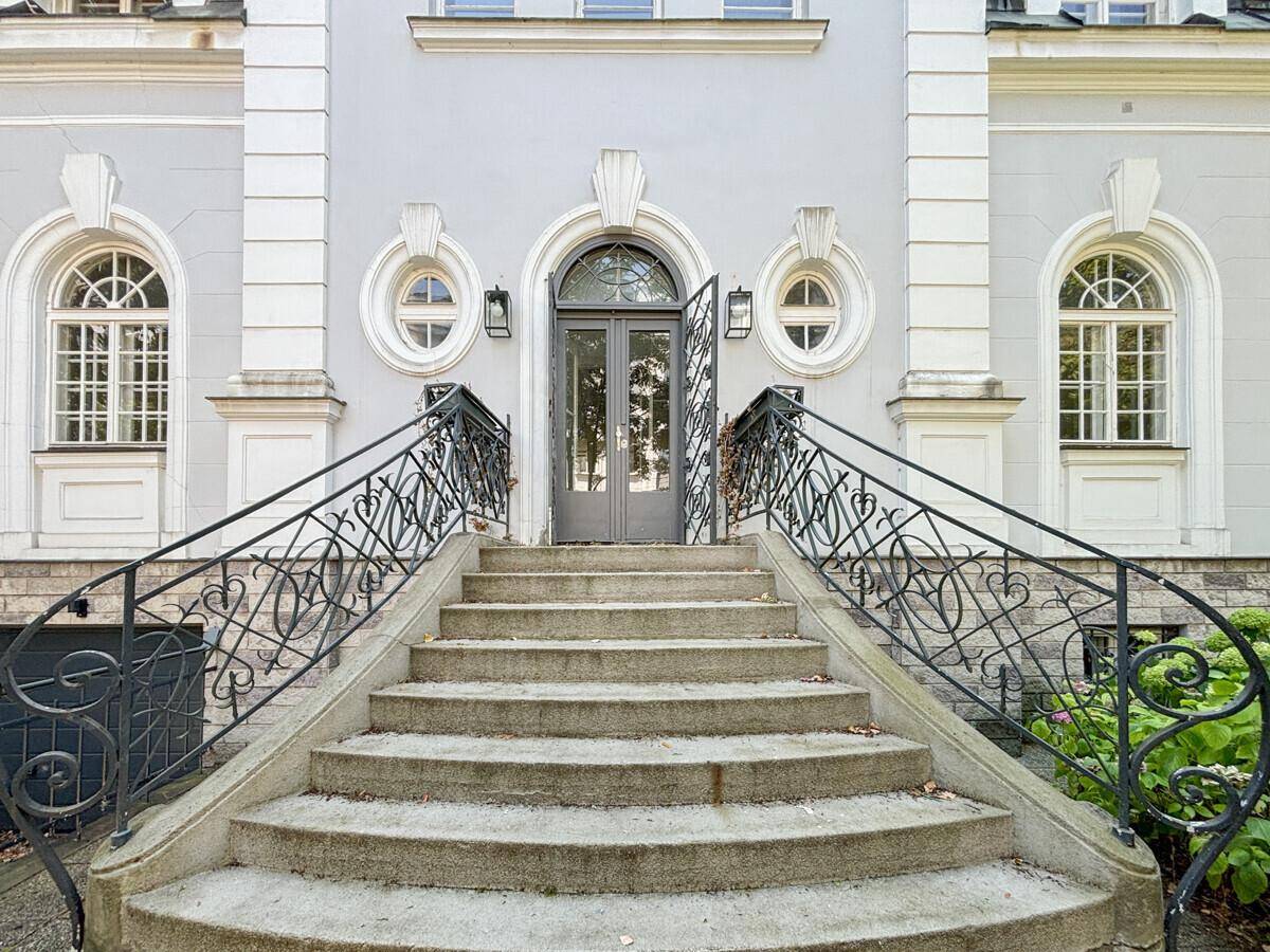 Repräsentativer Eingangsbereich des Gebäudes mit breiter Steintreppe und schmiedeeisernem Geländer.
