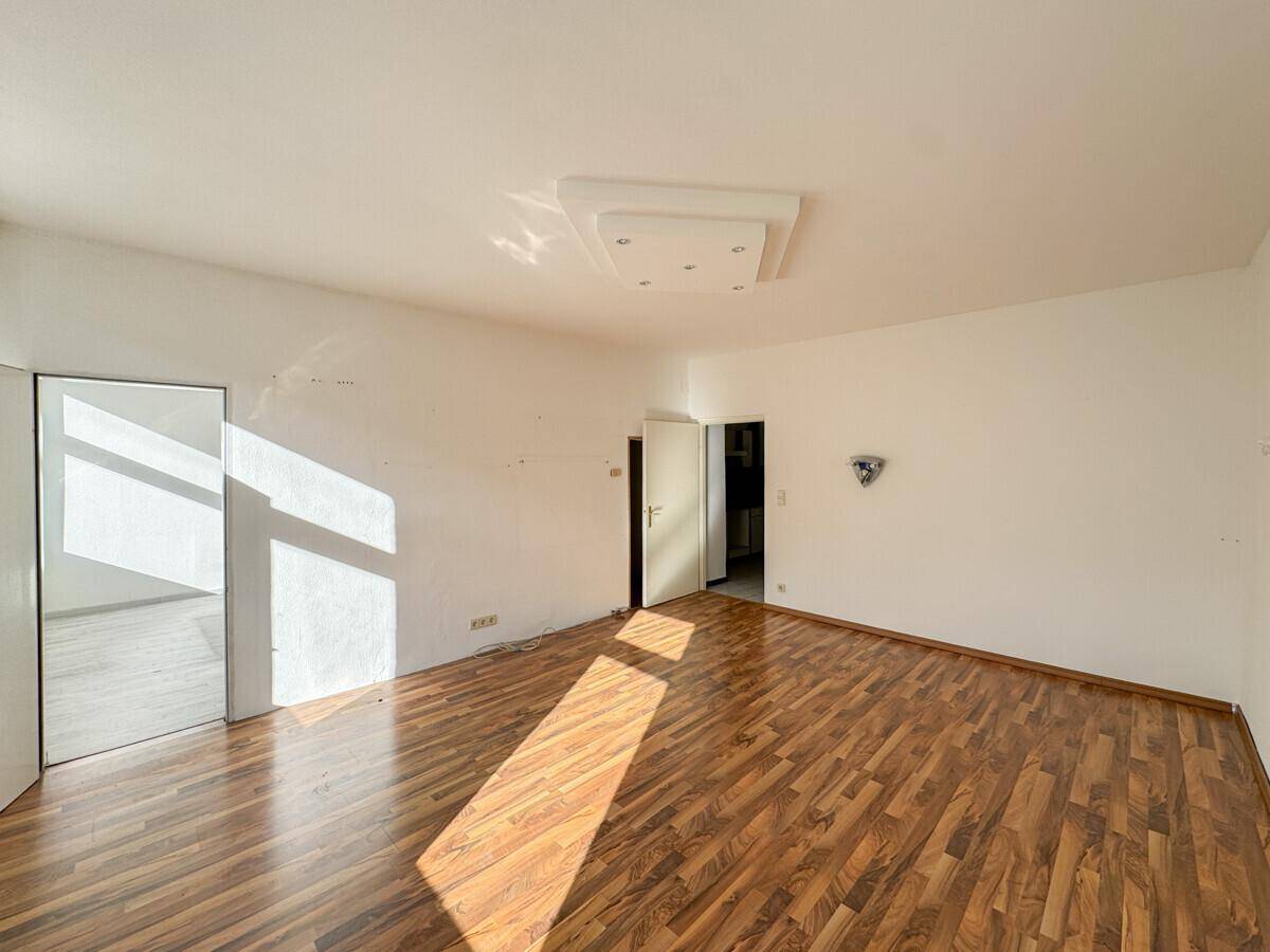 Geräumiges, leeres Zimmer mit Laminatboden und sonnigen Lichtflecken, ideal für neue Einrichtung.