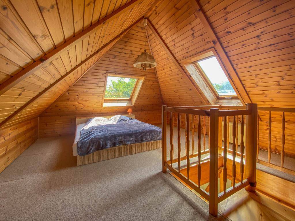Helles Dachboden-Schlafzimmer mit Holzverkleidung, Dachfenstern und einem Doppelbett.