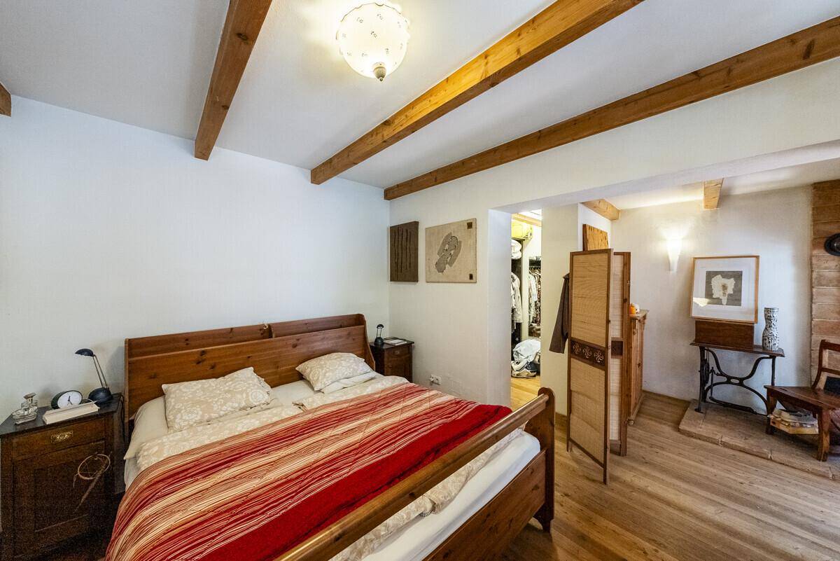Gemütliches Schlafzimmer mit Holzbett, sichtbaren Holzbalken und Parkettboden, mit Zugang zu einem Ankleidebereich.