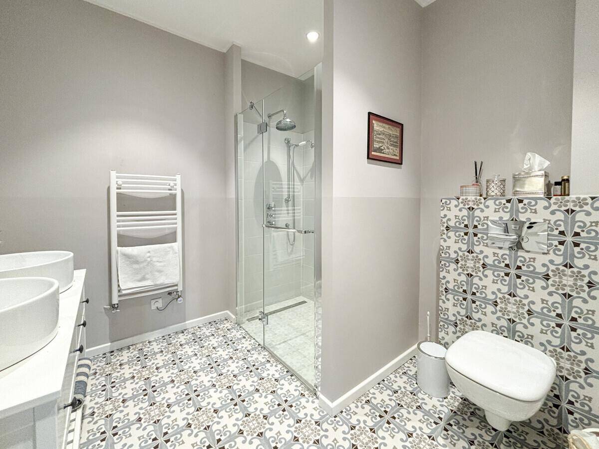 Modernes Badezimmer mit begehbarer Dusche, Doppelwaschbecken und stilvollen gemusterten Fliesen.