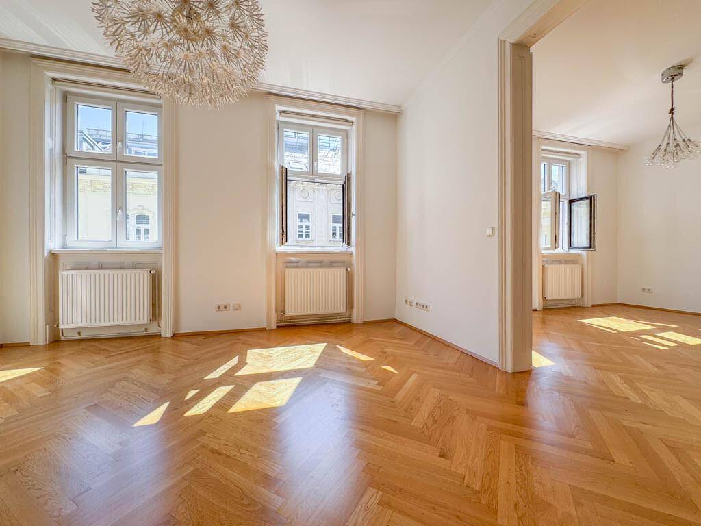 Großzügiges Wohnzimmer mit klassischem Fischgrätparkett, hohen Decken und viel Tageslicht.