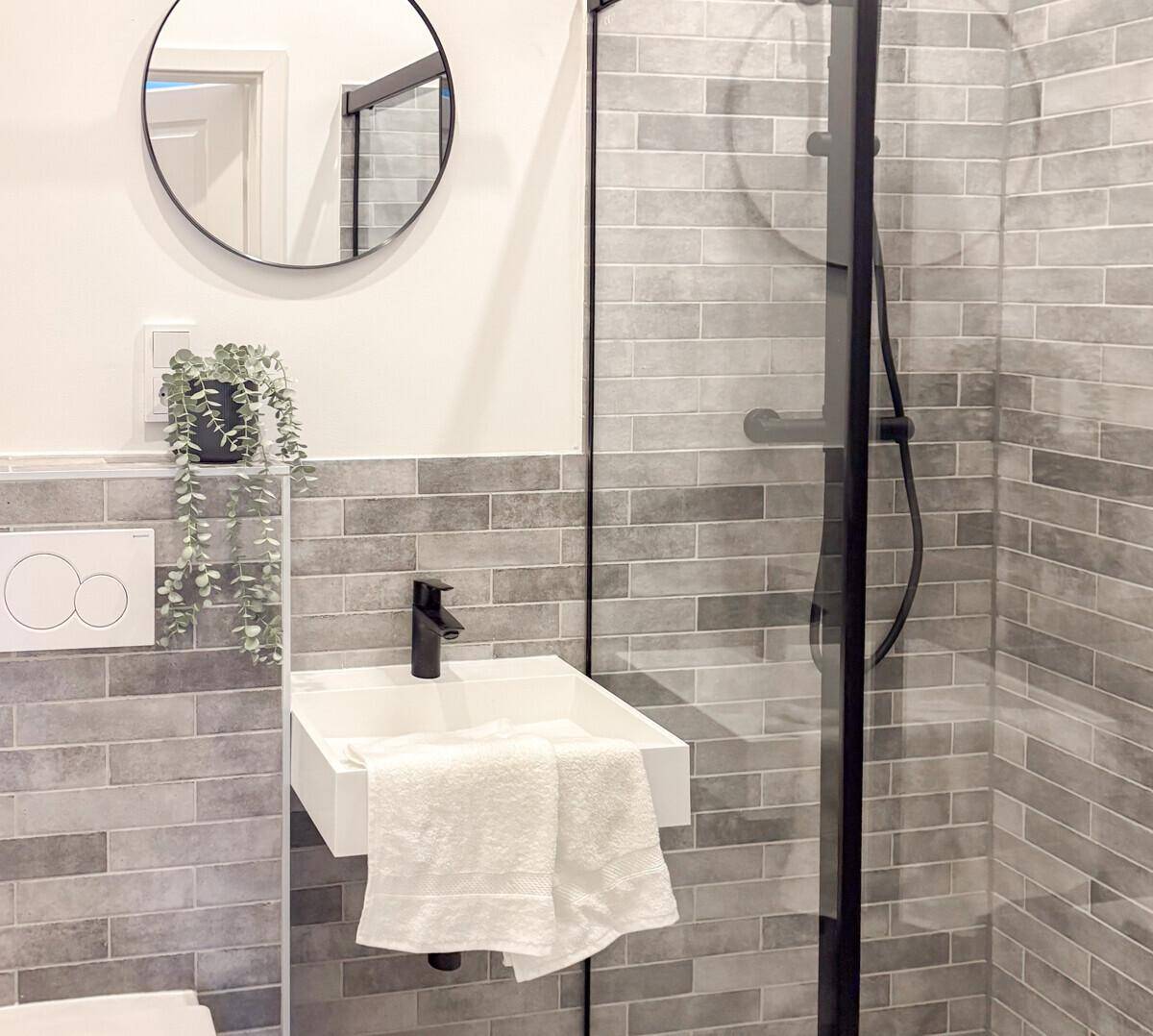 Modernes Badezimmer mit Duschkabine, Waschbecken und grauen Wandfliesen.