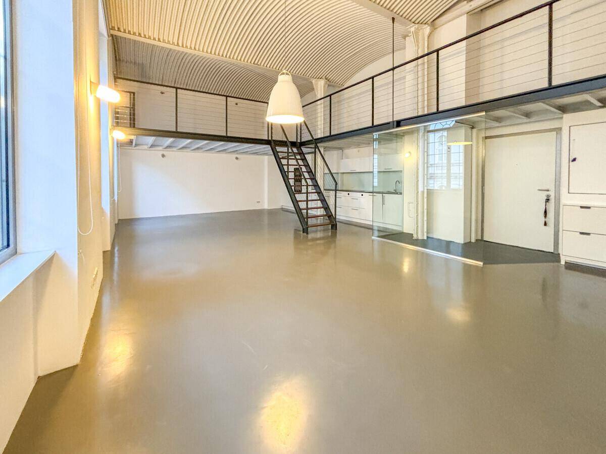 Heller Loft-Wohnbereich mit integrierter Küche, Galerie und industrieller Treppe.